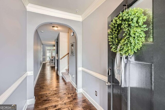corridor featuring arched walkways, wood finished floors, baseboards, ornamental molding, and stairs
