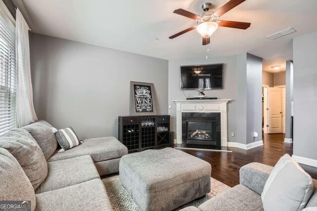 living area featuring visible vents, a glass covered fireplace, wood finished floors, baseboards, and ceiling fan
