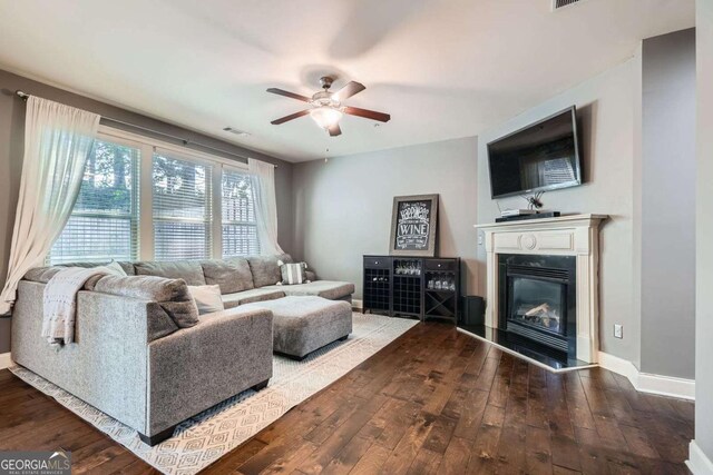 living area featuring a glass covered fireplace, a ceiling fan, dark wood-type flooring, and visible vents