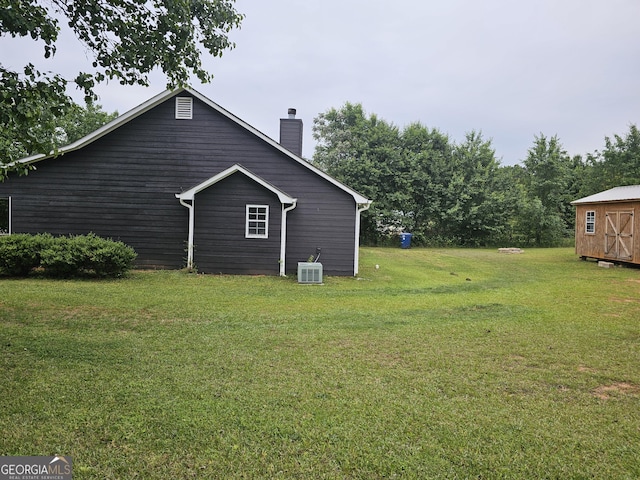 exterior space featuring central AC, a shed, a chimney, a lawn, and an outdoor structure
