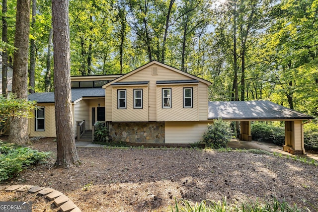 split level home with a shingled roof, stone siding, and a carport