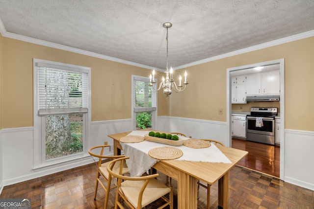 dining room with a textured ceiling, a chandelier, wainscoting, and ornamental molding