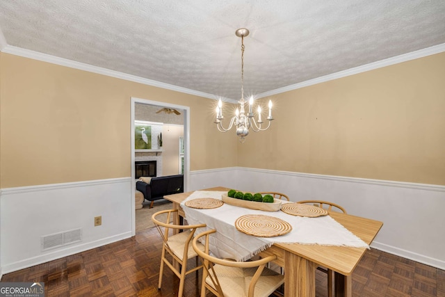 dining room featuring a fireplace, a textured ceiling, a chandelier, a wainscoted wall, and visible vents