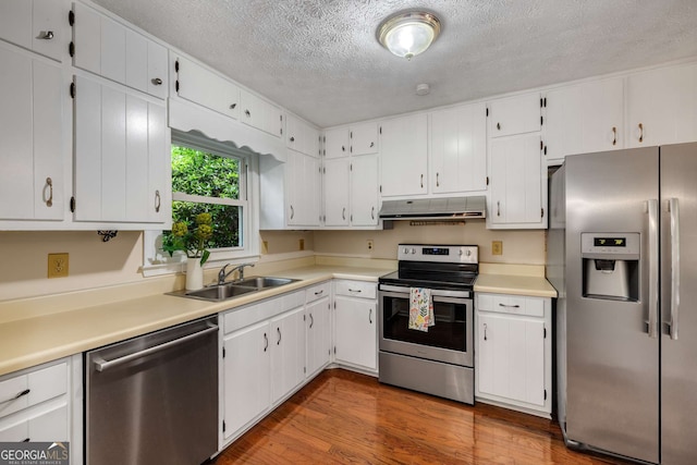 kitchen with a textured ceiling, under cabinet range hood, a sink, dark wood finished floors, and stainless steel appliances