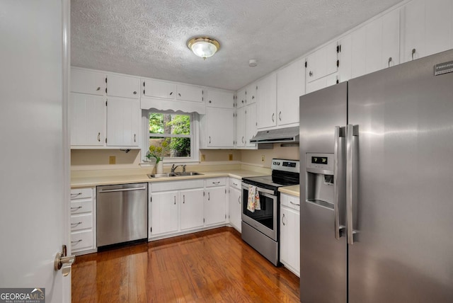 kitchen with dark wood-style flooring, a sink, light countertops, stainless steel appliances, and under cabinet range hood