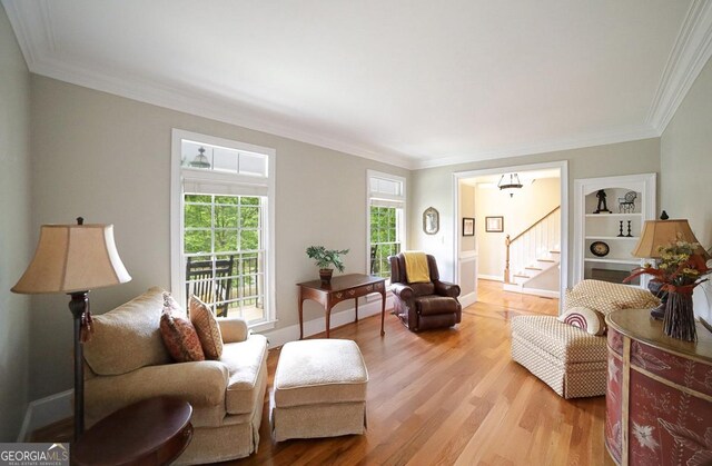 living room featuring light wood-style floors, crown molding, and stairway