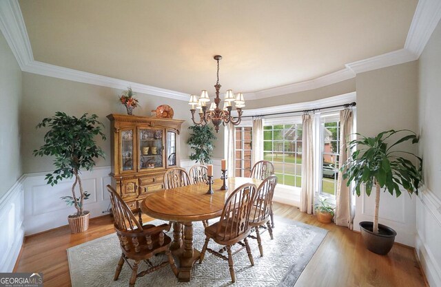 dining room with ornamental molding, a decorative wall, a wainscoted wall, a chandelier, and light wood-style flooring