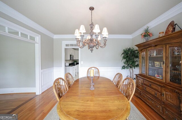dining room featuring crown molding, a notable chandelier, wood finished floors, and a wainscoted wall