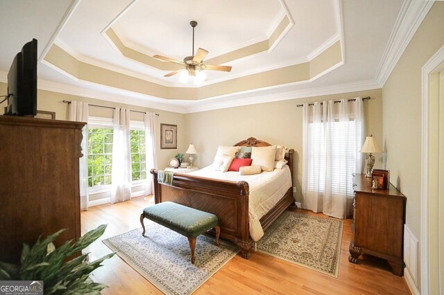 bedroom featuring a raised ceiling, ornamental molding, and light wood-type flooring