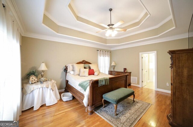 bedroom featuring light wood-style floors, ornamental molding, a tray ceiling, and visible vents