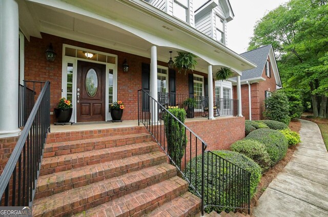 view of exterior entry featuring a porch and brick siding