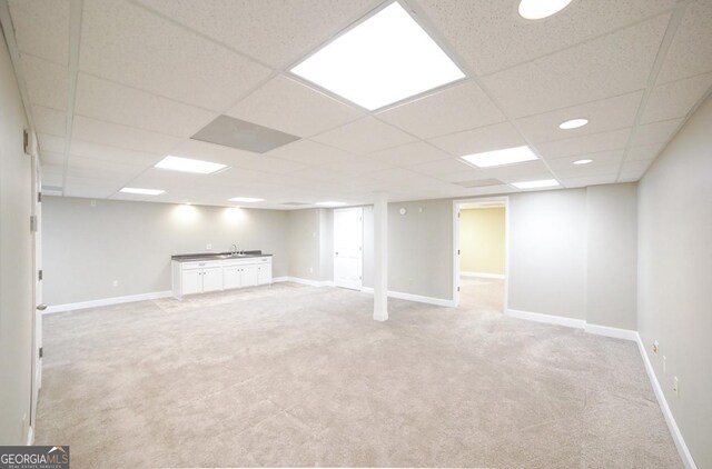 finished basement with a sink, baseboards, a drop ceiling, and light colored carpet