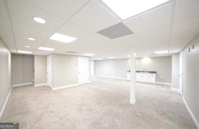 finished basement with baseboards, a sink, a paneled ceiling, and light carpet