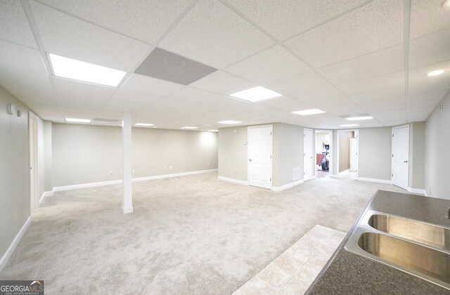 finished below grade area with baseboards, a sink, carpet, and a drop ceiling