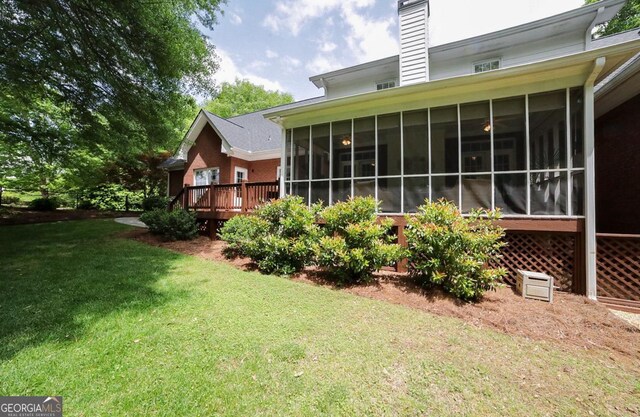 rear view of property featuring a yard, a deck, a chimney, and a sunroom