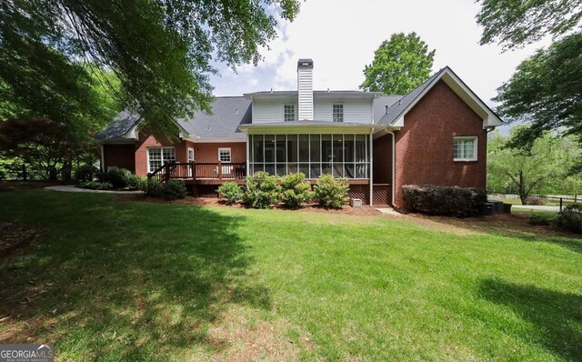 rear view of property with a chimney, a deck, a sunroom, brick siding, and a yard