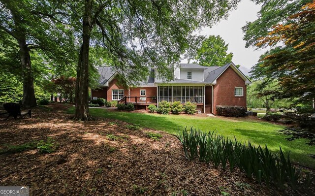 rear view of house featuring a yard, a wooden deck, and a sunroom