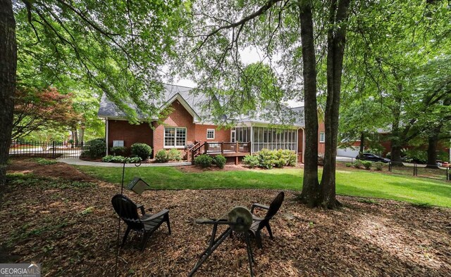 rear view of house with a yard, fence, a wooden deck, and a sunroom