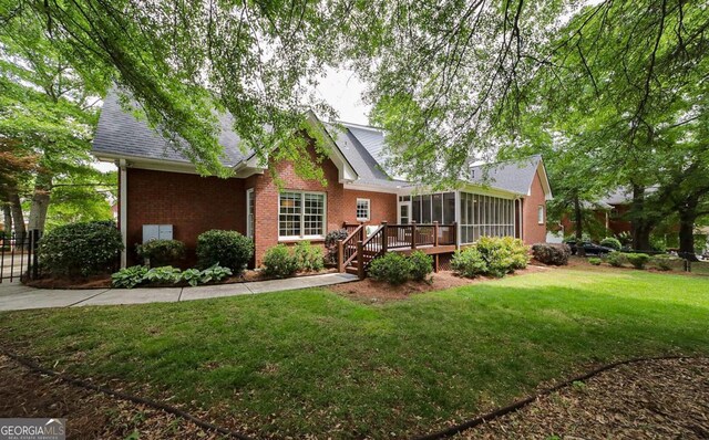 exterior space with a sunroom, roof with shingles, a front yard, and brick siding