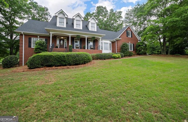 cape cod house featuring covered porch, brick siding, and a front yard
