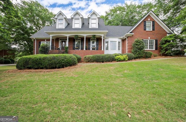 cape cod-style house featuring a porch, brick siding, and a front yard