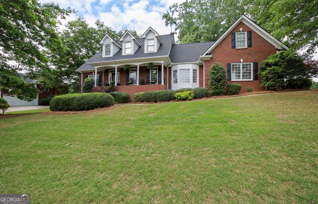 cape cod home with covered porch, brick siding, and a front yard