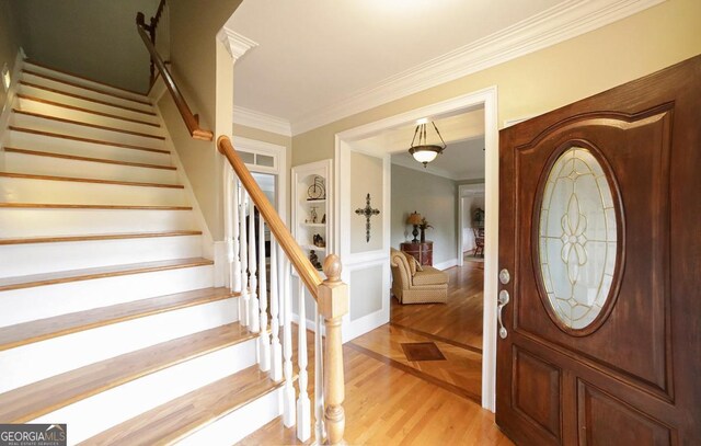 foyer entrance with light wood-style floors, baseboards, ornamental molding, and stairs