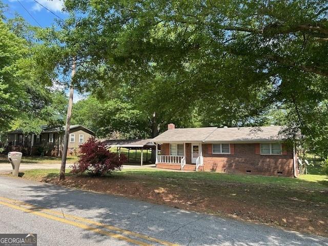 ranch-style house featuring a porch, a chimney, crawl space, and a carport