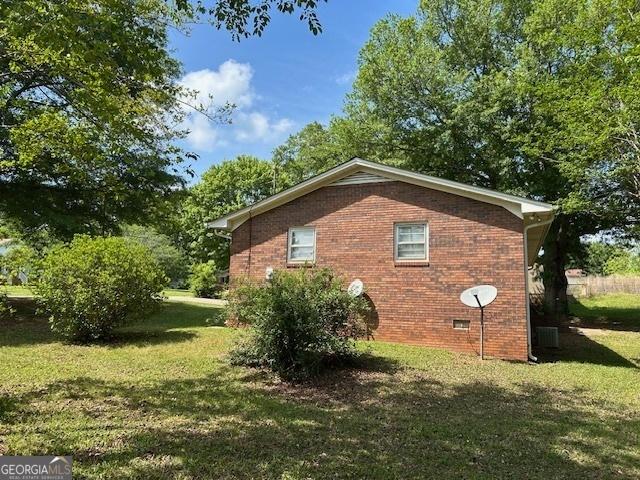 view of side of home with a lawn, brick siding, and crawl space