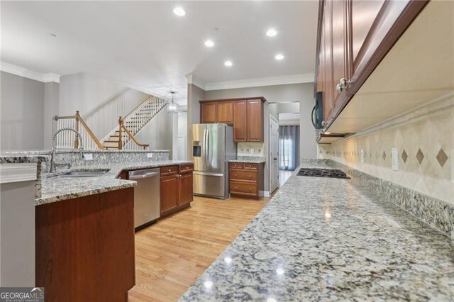 kitchen with crown molding, a sink, light wood-style flooring, stainless steel appliances, and tasteful backsplash