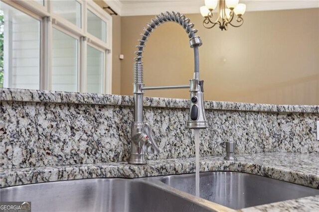 room details featuring stone countertops, an inviting chandelier, decorative backsplash, and a sink