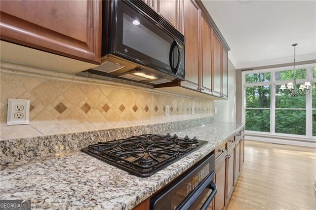 kitchen with pendant lighting, light stone countertops, tasteful backsplash, light wood finished floors, and black appliances
