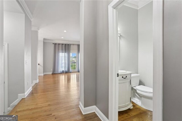 corridor with light wood-style floors, ornamental molding, baseboards, and recessed lighting