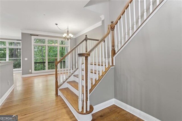 stairs featuring an inviting chandelier, baseboards, ornamental molding, and wood finished floors