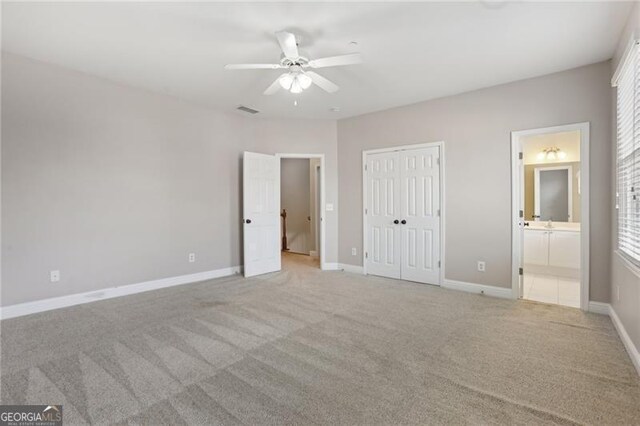 unfurnished bedroom featuring visible vents, a closet, baseboards, light colored carpet, and ensuite bath