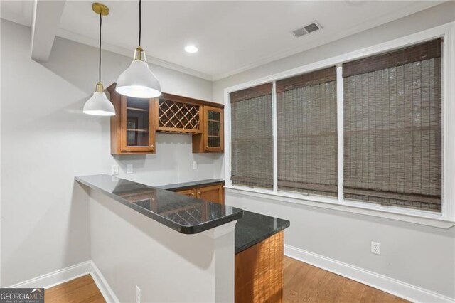 bar with visible vents, wood finished floors, baseboards, wet bar, and hanging light fixtures