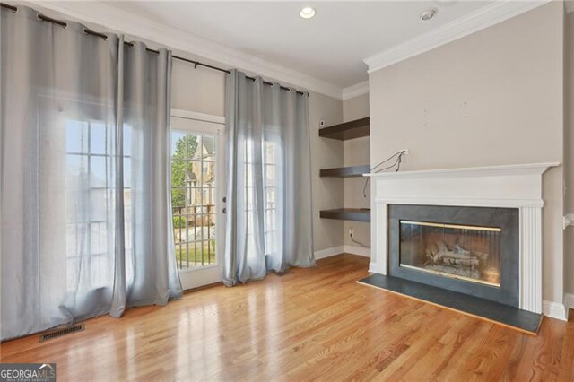 unfurnished living room featuring crown molding, visible vents, a glass covered fireplace, wood finished floors, and recessed lighting