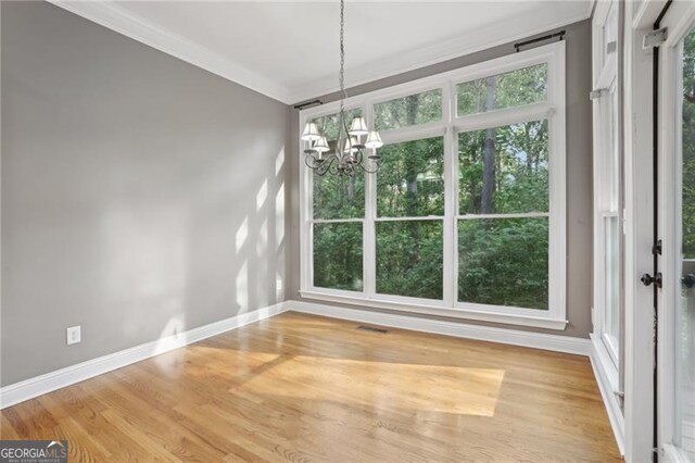 unfurnished dining area featuring visible vents, ornamental molding, an inviting chandelier, wood finished floors, and baseboards