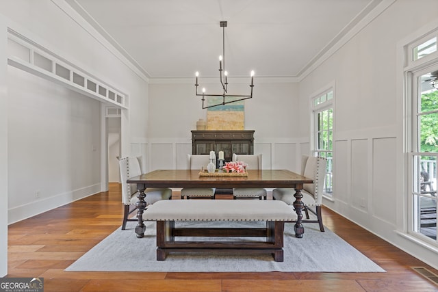 dining space with ornamental molding, a decorative wall, wood finished floors, and visible vents