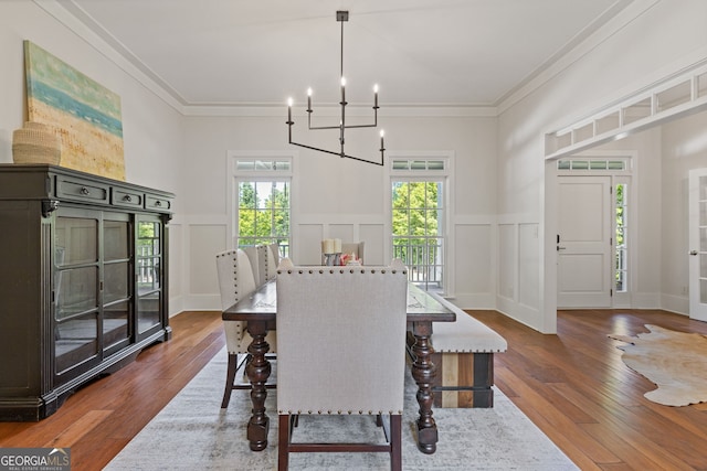 dining area with wood-type flooring, crown molding, a decorative wall, and a notable chandelier
