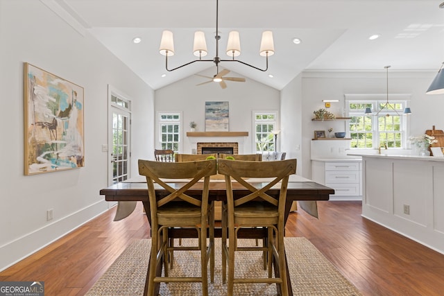 dining space featuring ceiling fan with notable chandelier, a brick fireplace, lofted ceiling, and dark wood-style floors