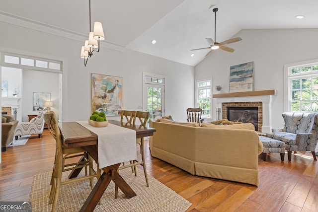dining area with a brick fireplace, light wood-style floors, ceiling fan, high vaulted ceiling, and recessed lighting