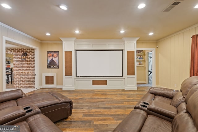 cinema with crown molding, a decorative wall, wood finished floors, and visible vents
