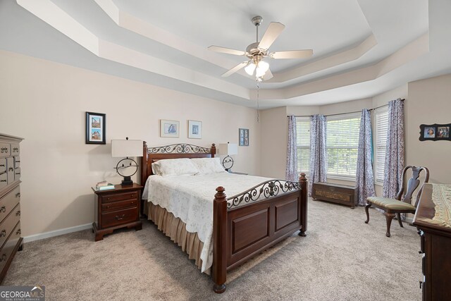 bedroom with a ceiling fan, baseboards, light colored carpet, and a raised ceiling