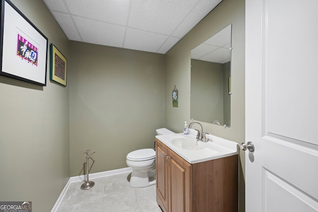 half bathroom with baseboards, vanity, toilet, and a paneled ceiling