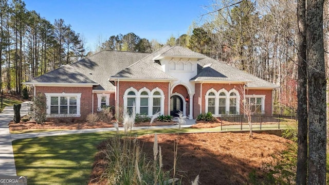 view of front of property featuring brick siding, roof with shingles, and a front lawn
