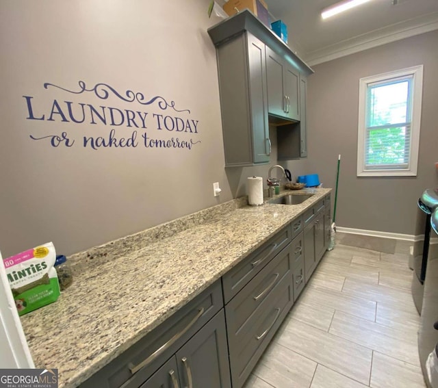 laundry area featuring washing machine and clothes dryer, cabinet space, a sink, baseboards, and ornamental molding