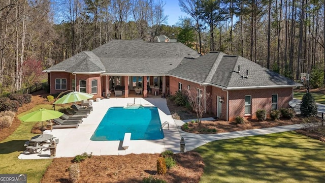 rear view of property featuring roof with shingles, a patio, an outdoor pool, and brick siding