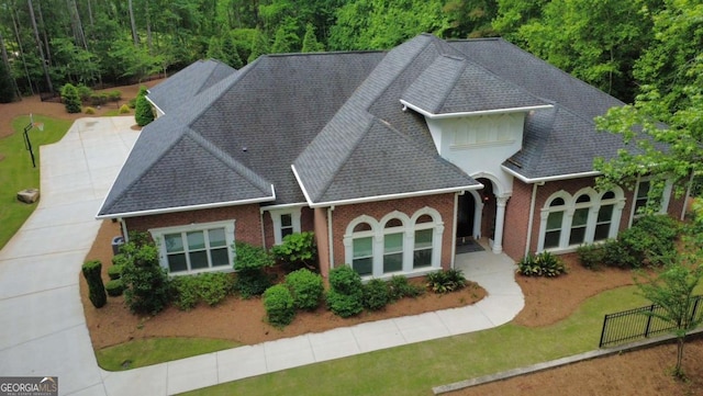 exterior space featuring brick siding, fence, roof with shingles, and a front lawn