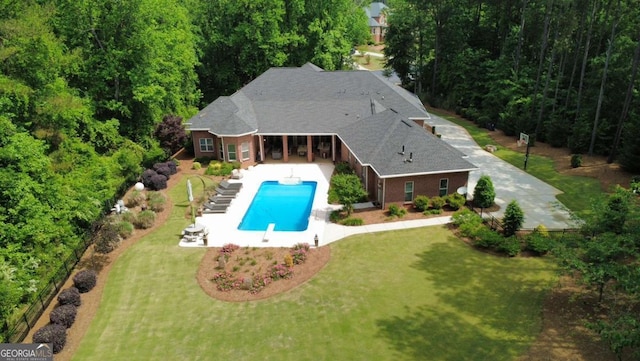 outdoor pool featuring a lawn, a view of trees, and a patio area